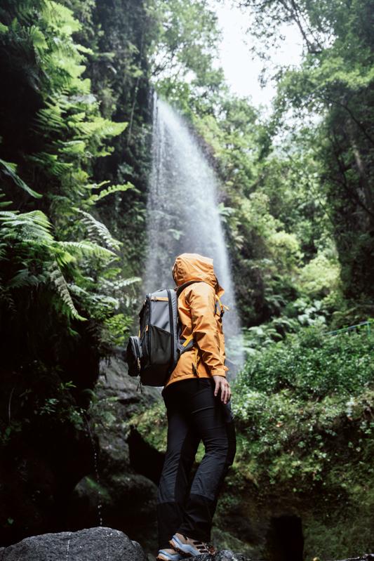 fotografía de producto persona llevando equipamiento de excursion en una zona boscosa con una cascada de fondo